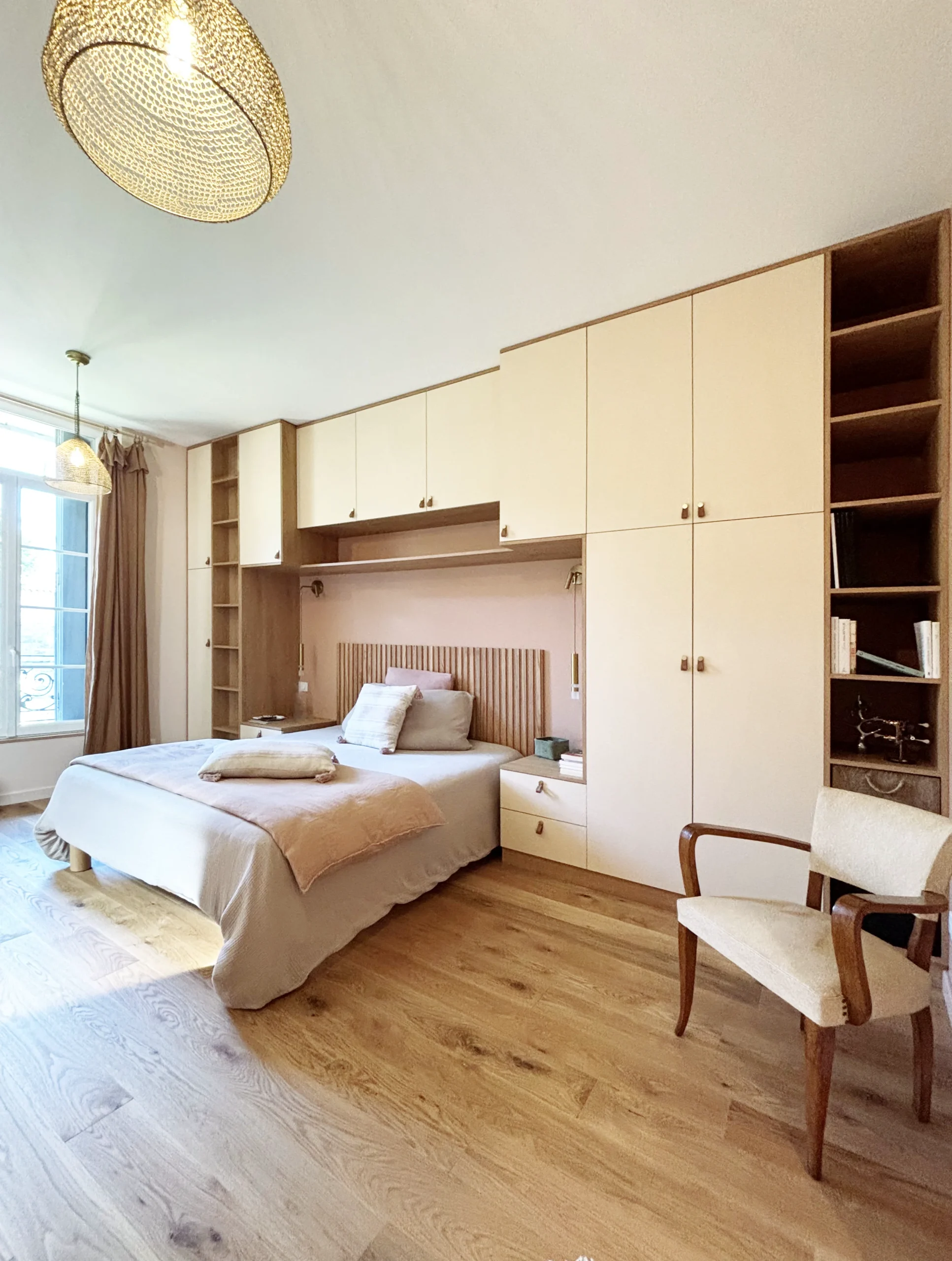 Chambre lumineuse avec lit, rangements intégrés, fenêtre avec rideaux et étagères ouvertes.