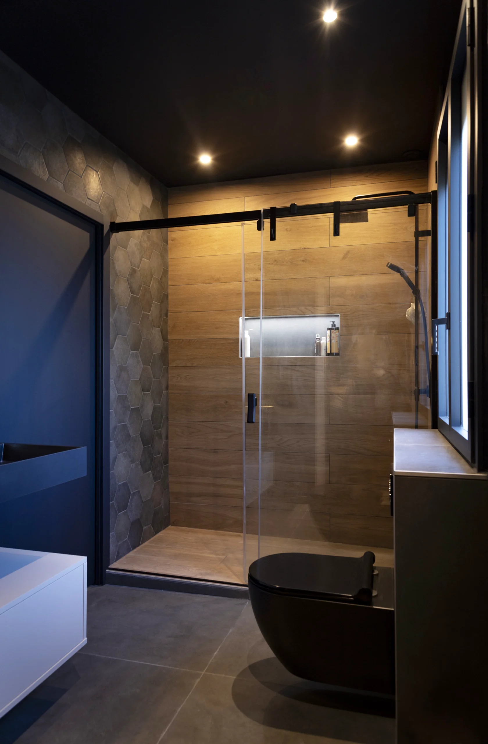 Douche vitrée contemporaine avec quincaillerie noire coulissante, équipement mural et WC noir.
