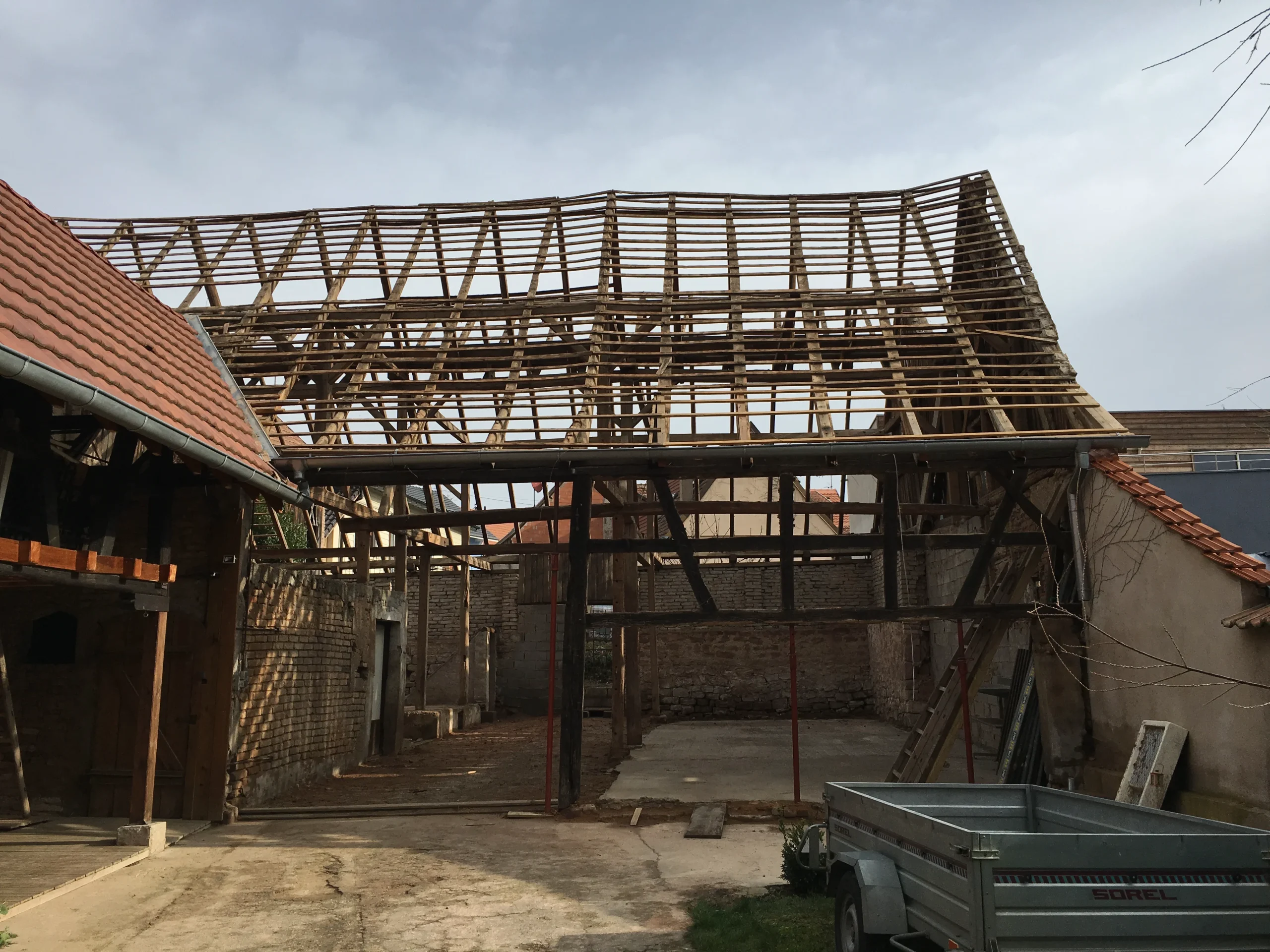 Structure de toit en bois apparente au-dessus d’une cour entre des bâtiments maçonnés.